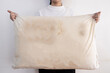 © Satjawat - Old pillow with yellow and dirty stains,woman holding a dirty pillow with sweat stains and saliva stains,accumulation of fungi, bacteria,germs or dust mites,unclean,unhygienic,health care concept.