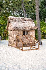 A small hut made of straw and wood sits on a sandy beach