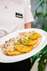 Wall Mural - A plate of delicious fried plantains topped with a creamy sauce and garnished with green onions, served by a person in a casual white shirt. Fresh and inviting, perfect for food lovers.