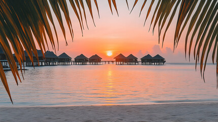 Wall Mural - Sunset over water bungalows on tropical beach, seen through palm fronds.