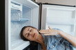 © SHOTPRIME STUDIO - A distressed woman in casual denim attire leaning against an open refrigerator, expressing discomfort and fatigue, highlighting issues of mood and energy depletion