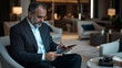 © stock1 - An executive sitting in a luxury office lounge, working on a tablet. The background features modern furniture, a coffee table, and soft ambient lighting