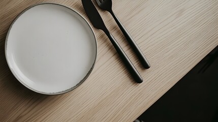 Poster - A closeup of a light oak countertop with a matte white plate and black metal cutlery, showcasing Scandinavian minimalism