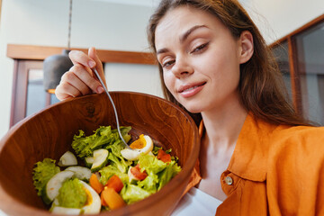 Canvas Print - Young woman smiling while holding a bowl of fresh salad, dressed in a casual orange shirt, showcasing healthy eating lifestyle in a bright indoor setting