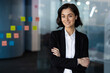 © Liubomir - Confident woman in business attire standing with arms crossed in modern office, smiling. Represents leadership, success, and empowerment in professional environment.
