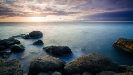 Poster - A rocky shoreline with a body of water in the background. The water is calm and the sky is cloudy