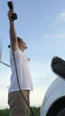 Wall Mural - Progressive man with his electric car, EV car recharging energy from charging station on green field with wind turbine as concept of future sustainable energy. Electric vehicle with energy generator.