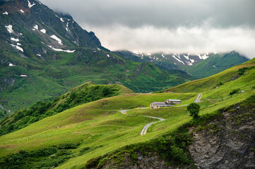 Wall Mural - LES CHAPIEUX , Alps, France, Tour du Mont Blanc - the mountain shelter and farm near Cormet de Roselend  with high peaks in background and a winding road
