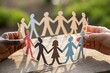© Realistic Moments - Silhouettes of diverse paper figures on hands symbolizing inclusion and equality, set against a bright background.