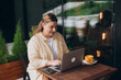 © mdyn - Happy 30s woman doing business on laptop and smiles. Young woman enjoy her work outdoor. Remote work, freelance. Cheerful programmer works remotely on laptop and try to meet deadline outdoor in cafe.