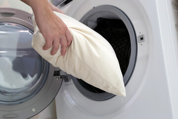 Man's hand holds a pillow and puts it in the washing machine.