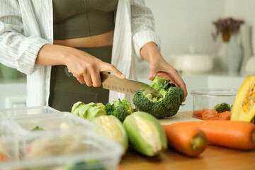 Wall Mural - Young sporty woman chopping fresh broccoli on cutting board preparing containers of healthy food. Healthy eating and a balanced lifestyle concept.