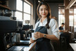 © RooftopStudioBangkok - pretty barista holding cup in cozy cafe setting, with warm smile and stylish apron. background features coffee machines and relaxed atmosphere