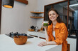 © SHOTPRIME STUDIO - Cheerful young woman with long hair wearing a bright orange shirt enjoying green smoothie in a modern kitchen, promoting healthy lifestyle and nutritious eating