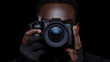 © KAMOLPOP - Photographer in Shadow: A close-up shot of a photographer's hands holding a professional camera, their face partially obscured in shadow against a dark background.