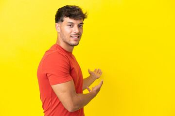 Sticker - Young caucasian handsome man isolated on yellow background extending hands to the side for inviting to come