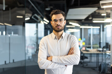 Poster - Mature man businessman confidently stands with arms crossed in a modern office environment. The subject portrays professionalism, ambition, and determination, epitomizing a successful corporate image