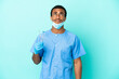 © luismolinero - African American dentist holding tools over isolated blue background and looking up