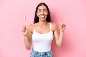 Wall Mural - Young caucasian woman brushing teeth isolated on pink background pointing up a great idea