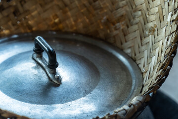 Close up of traditional aluminum pot lid with black handle and woven bamboo basket, rustic kitchen theme