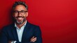 © svastix - A smiling man with stylish glasses poses confidently with arms crossed in front of a striking red backdrop, conveying optimism and professionalism.
