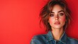 © svastix - A stylish woman with short hair in a denim jacket poses confidently against a vivid red backdrop, highlighting her strong and fashionable presence.