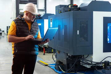 Poster - man near industrial equipment. large milling machine behind worker. man with laptop stands inside wo