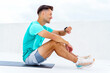 © muse studio - Man checking fitness watch while sitting on mat in an outdoor setting during a cloudy day