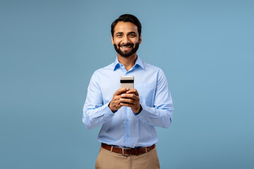 Portrait of smiling, happy bearded middle aged Indian man holding mobile phone, using mobile app