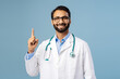 © Maria Vitkovska - Portrait of handsome, smiling, Indian man wearing white coat, stylish eyeglasses pointing finger up