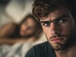 © Aodsy - Intense Close-Up of a Young Man with Striking Eyes in a Softly Focused Bedroom Scene with a Woman in the Background Showing a Hint of Emotion and Tension