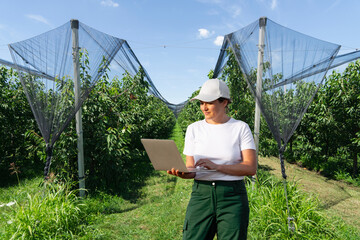 Aufkleber - Farmer controls conditions in the garden of fruits and sends data to the cloud from the laptop. Smart farming and digital agriculture.