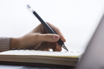 Poster - Close perspective of a woman's hand making entries in a notepad on a cutting-edge laptop, with a soft blur in the surrounding