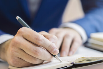 Poster - A man's hand inscribing in a notepad, captured closely, with a vague background