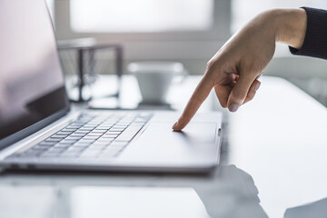 Poster - A detailed view of female hands typing on a cutting-edge laptop keyboard, set against a hazy office backdrop
