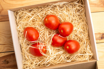 Wall Mural - Fresh juicy tomatoes in a box with shavings on a wooden table, close-up, top view.