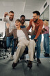 © Zamrznuti tonovi - Business colleagues pushing businesswoman on office chair, having fun and celebrating success
