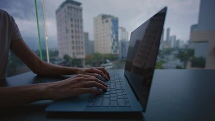 A female programmer works on a laptop overlooking a rainy city.