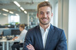 © Igor - Confident young business man with crossed arms in a professional office setting, showcasing a bright smile and formal suit, surrounded by a modern workplace environment.
