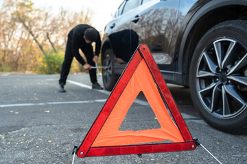 A man changes a car tire, a sign of an emergency situation.