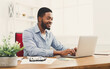 © Prostock-studio - Happy black businessman working on laptop in modern white office interior. Smiling employee at work with computer, copy space