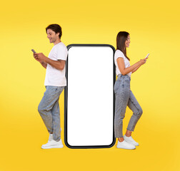 Wall Mural - Great App. Excited Couple Leaning On Big Smartphone With Blank White Screen Using Cell Phones, Cheerful Guy And Lady Chatting On Social Media, Standing On Yellow Orange Background, Mock Up, Full Body