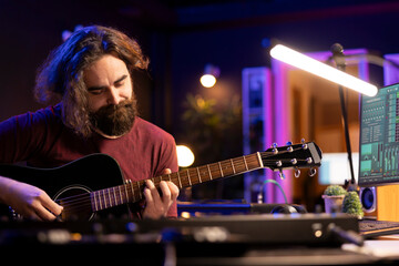Fototapete - Songwriter musician recording sounds on daw software with guitar, enjoying leisure time in home studio office. Audio engineer and producer creating new songs, electronic mixing instruments.