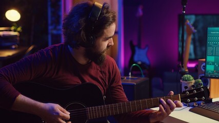 Fototapete - Sound engineer playing acoustic guitar and using mixing console to record music, adjusting volume and adding sound effects to tunes. Artist works with digital audio workstation software. Camera A.