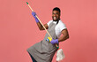 © Prostock-studio - Portrait Of Funny Black Man In Apron With Mop In Hands Posing Over Pink Studio Background, Using Handle As Guitar, Fooling With Household Tool