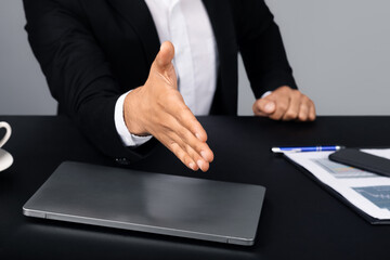 Poster - Cropped of entrepreneur in a suit offers a handshake across a desk with a laptop and documents. The setting reflects a modern corporate environment, emphasizing professional interaction.
