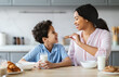 © Prostock-studio - A loving mother shares a cookie with her delighted son in their cozy kitchen. They bond over milk and laughter, capturing the essence of family togetherness and affection.