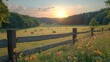© gentho - A serene sunset over a grassy field with hay bales and a wooden fence.