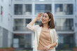 © amnaj - Asian businesswoman shielding her eyes while smiling and looking away in front of modern office building