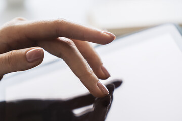 Poster - Closeup view of a woman's finger operating a high-tech tablet on a desk, amidst the blurred backdrop of a luminous office scene